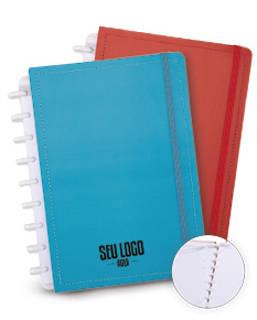 Caderno de Disco em branco com capa listrada amarela e textura de couro aberto em cima de uma pilha de papéis e notas, com um caderno aberto ao lado.